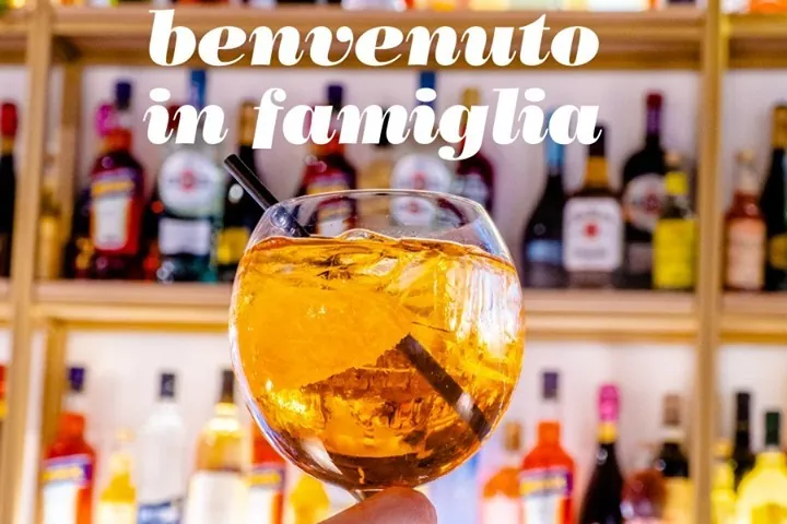 Verre de spritz levé devant les bouteilles du bar