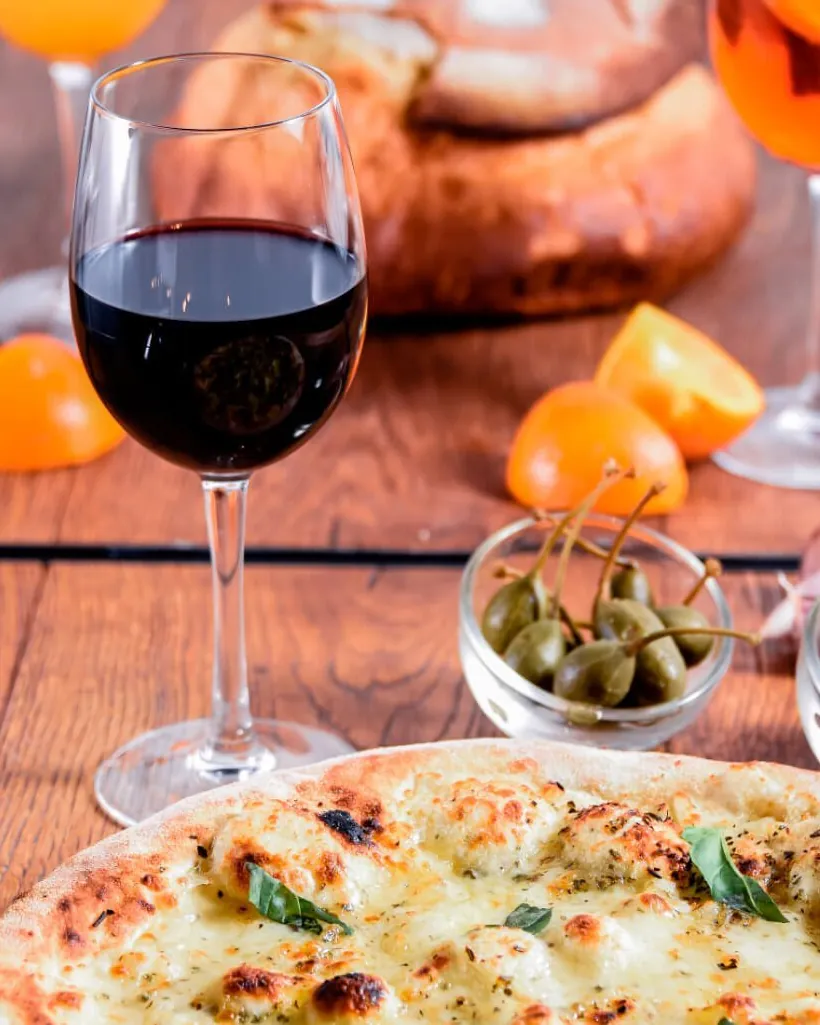 Pizza bianca au basilic, verre de vin rouge et câpres sur une table en bois de la trattoria